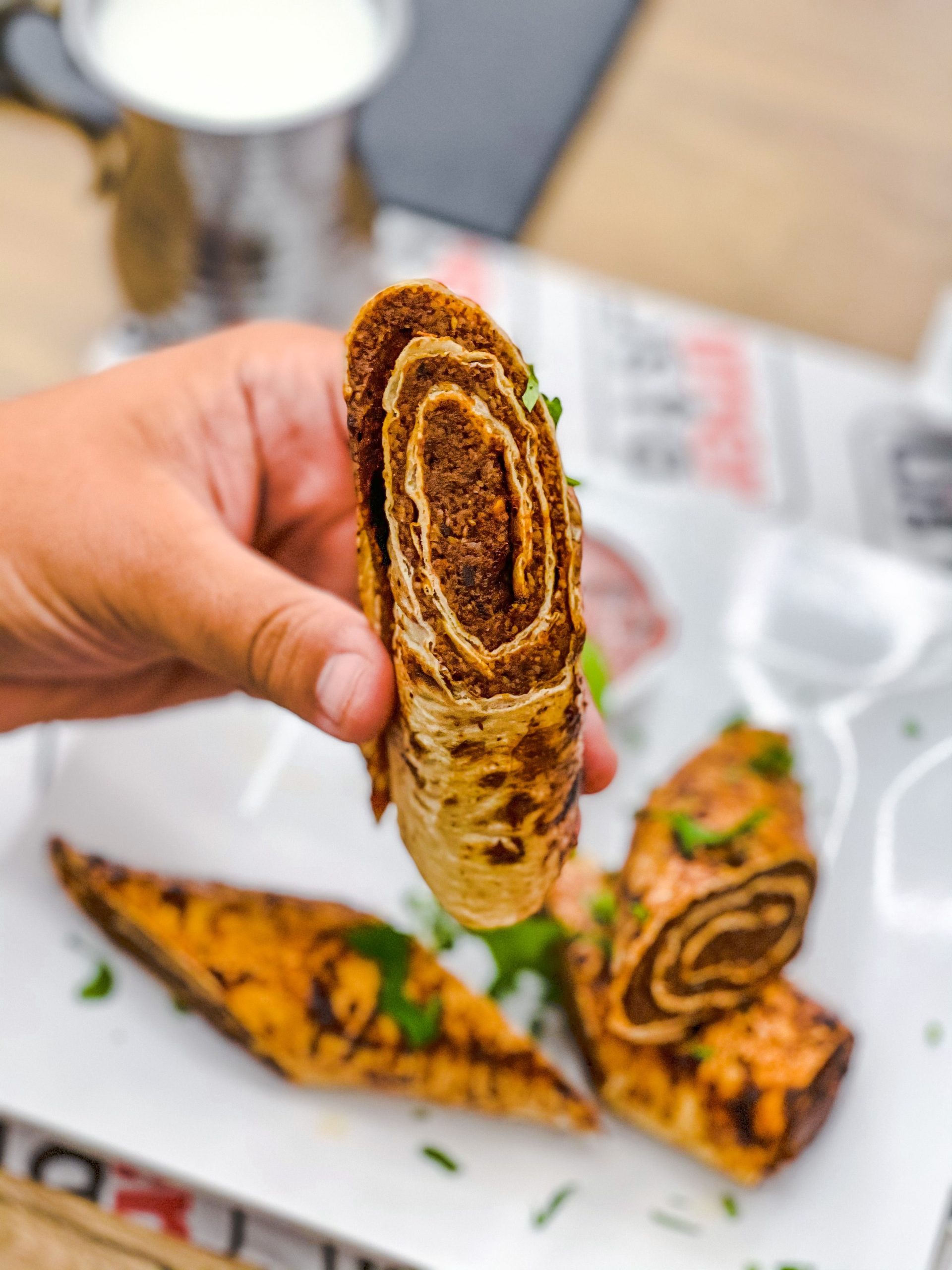 Nahaufnahme einer Hand, die eine köstliche, mit Fleisch gefüllte Tortilla-Rolle hält.